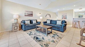 A spacious living room with two blue sofas, a coffee table, and a patterned rug. - Beachfront home with screened porch with boardwalk access to pool (Cape San Blas)