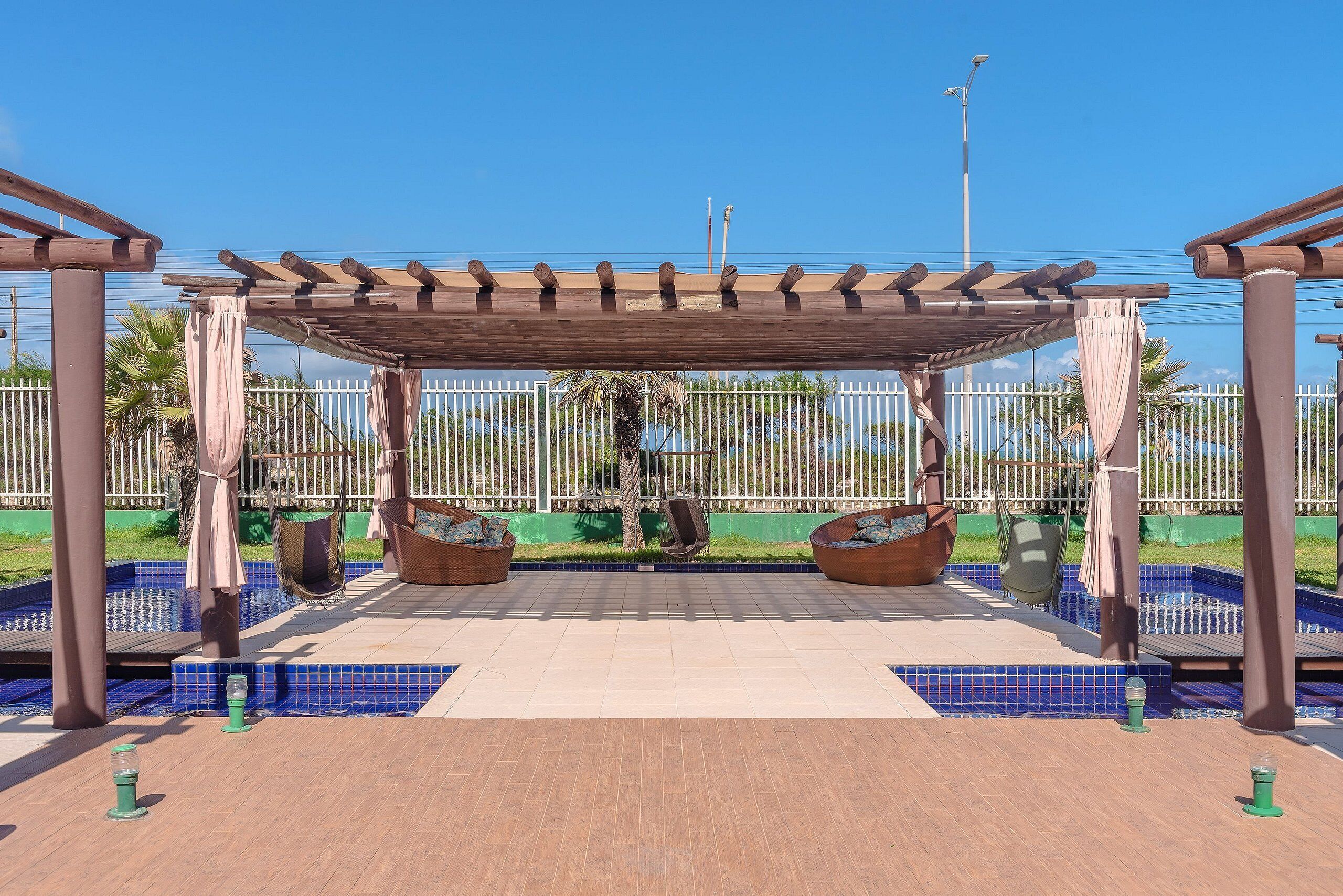 A covered outdoor seating area with a pergola, two swing chairs, and a tiled pool area.