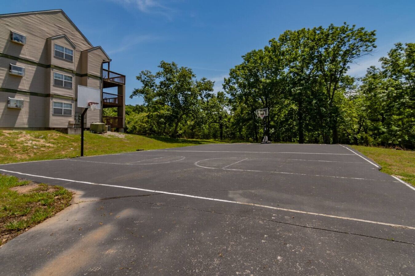 A basketball court with a basketball hoop, surrounded by trees and a building with a balcony.