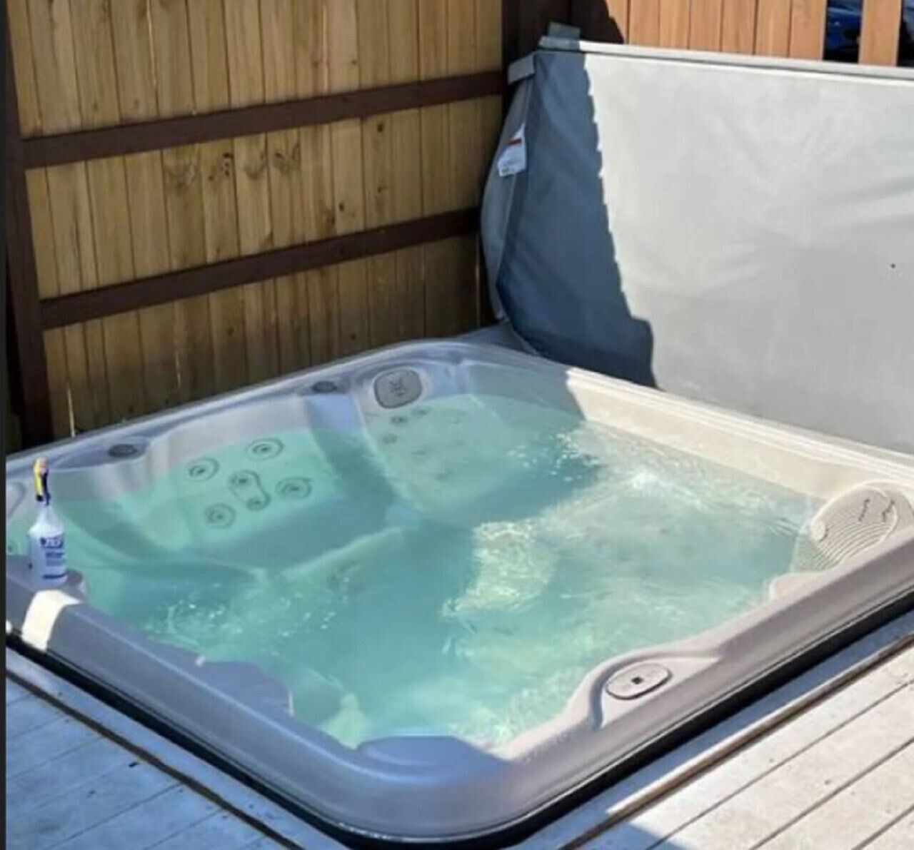Un jacuzzi con una botella de champán, rodeado de terrazas de madera y una valla de madera.