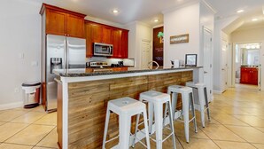 A modern kitchen with wooden cabinets, stainless steel appliances, and a bar area with stools. - Large, Open Home, Shared Pool, Bike or Walk to the Gulf (Destin)