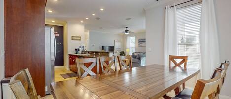 A spacious dining area with a wooden table and chairs, a kitchen in the background, and a ceiling fan.