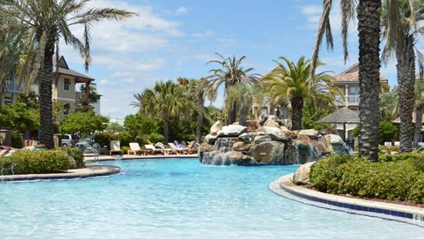 A resort pool with palm trees, lounge chairs, and a waterfall feature. - Large, Open Home, Shared Pool, Bike or Walk to the Gulf (Destin)