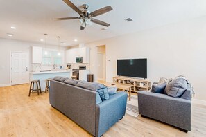 A modern living room with a grey sofa, a TV, and a ceiling fan.