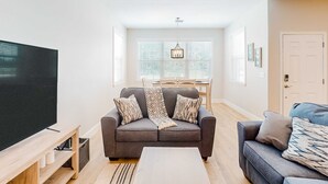Ein modernes Wohnzimmer mit einem grauen Sofa, einem weißen Couchtisch und einem Flachbildfernseher auf einem Holzgestell.