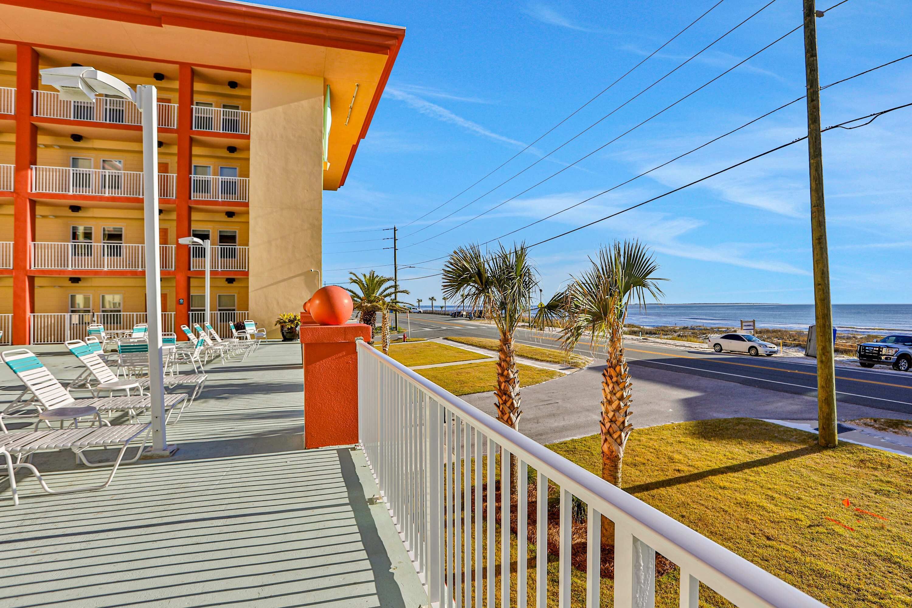 A hotel balcony with lounge chairs, a view of the ocean, and a road with cars.