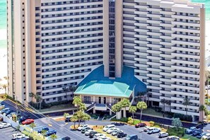Ein Hochhaus-Hotel mit mehreren Etagen, einem zentralen Innenhof und einem Parkplatz mit einigen Autos.