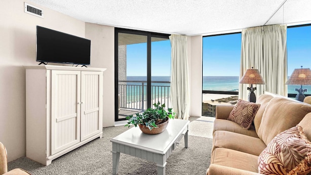Une chambre d’hôtel avec un téléviseur posé sur un meuble, un canapé, une table avec une plante et une vue sur la plage.