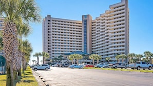 Un hôtel à plusieurs étages, doté d’un design moderne, avec un atrium central surmonté d’un toit bleu et un parking pouvant accueillir plusieurs voitures.