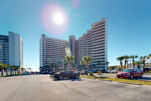 A parking lot with several cars, palm trees, and modern high-rise buildings in the background. - 14th Floor Airy Condo, On-site bar & restaurant, Pool w splash pad (Destin)