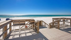 Une terrasse en bois avec des chaises en métal donnant sur une plage.