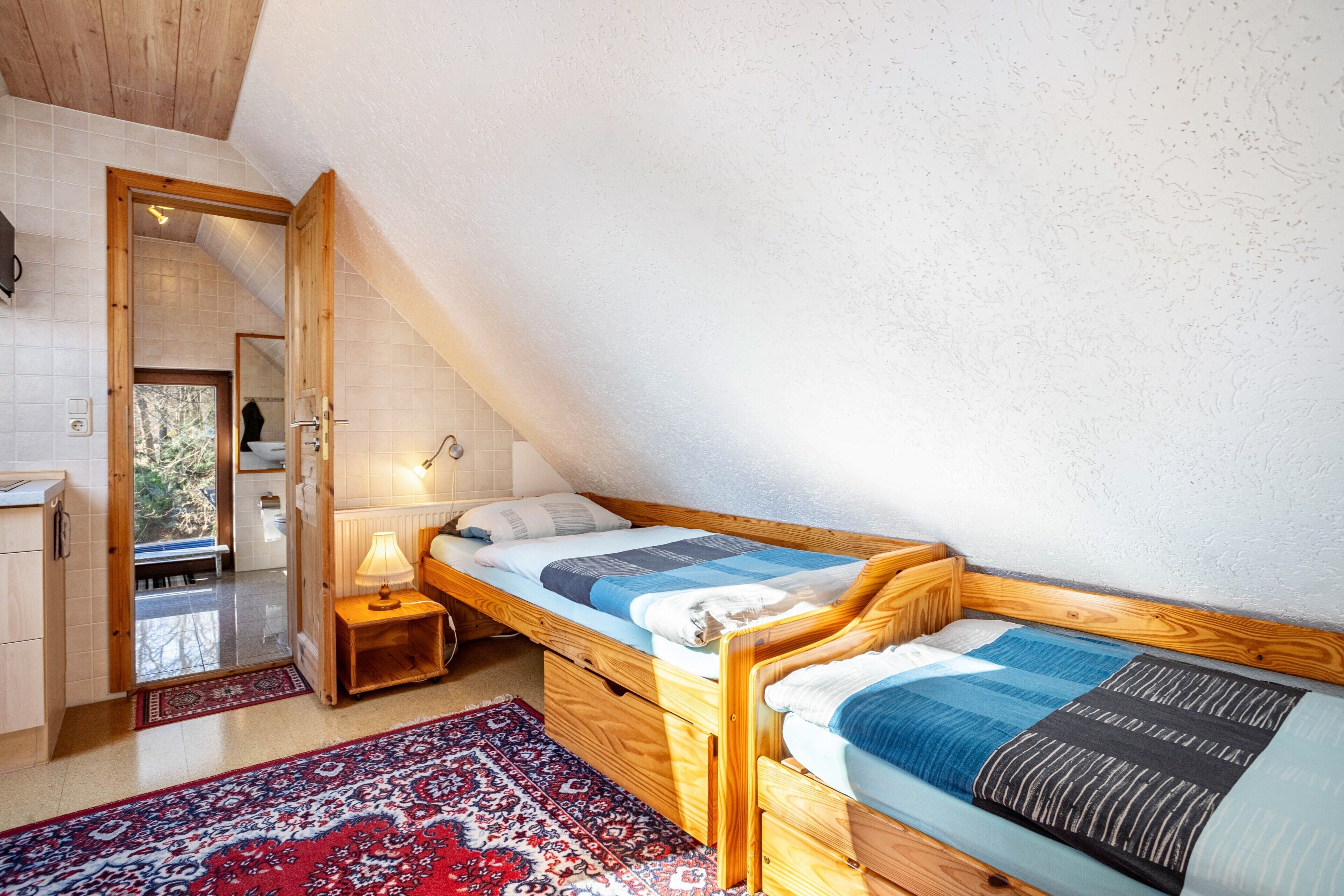 Camera da letto con letto a soppalco, comodino in legno, lampada e vista sull'esterno.