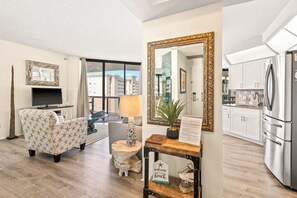 A modern living room with a sofa, a TV, a lamp, and a large mirror. - Gulf view condo w/ shared pool, hot tub, tennis, gym & easy beach access (Miramar Beach)