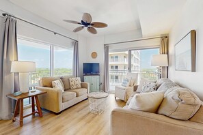 A spacious living room with a ceiling fan, large windows, and a view of the city. - Gorgeous coastal condo with shared pool and private balcony (Miramar Beach)