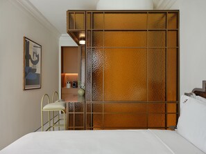 A hotel room with a bed, a desk, a chair, a painting, and a decorative partition. - The Newel Kolonaki (Athens)