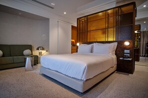 A modern hotel room with a large bed, a sofa, a nightstand, and a decorative wall panel. - The Newel Kolonaki (Athens)