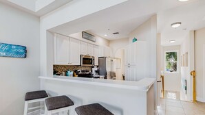 Une cuisine moderne avec des meubles blancs, un îlot central doté de tabourets et un panneau décoratif au mur.