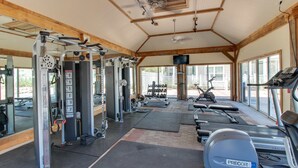 Une salle de sport équipée de divers appareils d’exercice, notamment des tapis de course et des appareils de musculation, le tout sous une structure de toit en bois.
