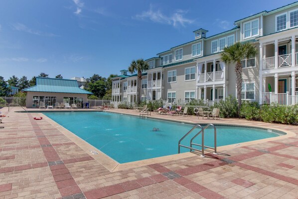A swimming pool area with a tiled deck, lounge chairs, and a building with balconies. - Bright, Airy Condo with Shared Outdoor Pool, High-Speed WiFi, and Central AC (Santa Rosa Beach)