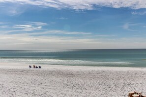 A beach with white sand and a clear blue sky. There are a few beach chairs and a small structure in the distance. - Bright, Airy Condo with Shared Outdoor Pool, High-Speed WiFi, and Central AC (Santa Rosa Beach)