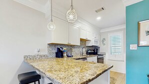Una cocina con armarios blancos, encimera de granito e iluminación colgante.