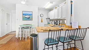 A compact kitchen with white cabinets, a wooden island, and bar stools. - Coastal Condo with heated pool, hot tub, tennis, & beach access (Destin)