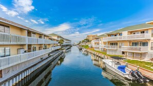 A canal with a boat docked on the right, surrounded by multi-story buildings with balconies and a clear sky. - Coastal Condo with heated pool, hot tub, tennis, & beach access (Destin)