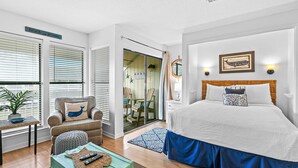 A bedroom with a bed, a chair, a table, and a green trunk. - Coastal Condo with heated pool, hot tub, tennis, & beach access (Destin)