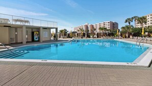 A swimming pool with a tiled deck, surrounded by palm trees and a building with multiple balconies. - Inlet Reef 414 (Destin)