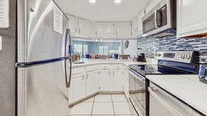 A modern kitchen with white cabinetry, a stainless steel refrigerator, a built-in oven, and a microwave. - Inlet Reef 414 (Destin)