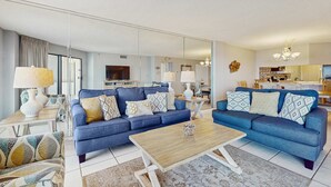A modern living room with two blue sofas, a wooden coffee table, and a large mirror reflecting the space. - Inlet Reef 414 (Destin)