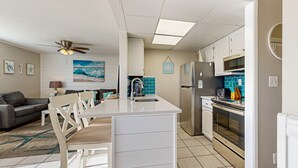 A compact kitchen with a central island, a dining area with chairs, a sofa, and a ceiling fan. - Inviting condo with dock, pool, hot tub & private beach - dog-friendly (Destin)