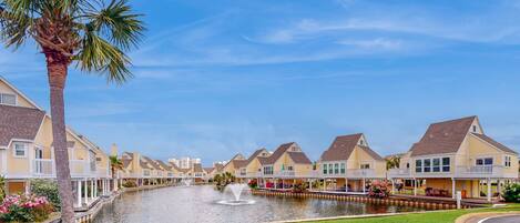 A waterfront property with a canal, houses with balconies, and a palm tree.