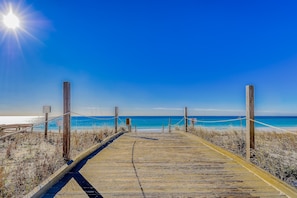 Un muelle de madera que conduce a una playa con agua azul cristalina y un sol brillante en el cielo.