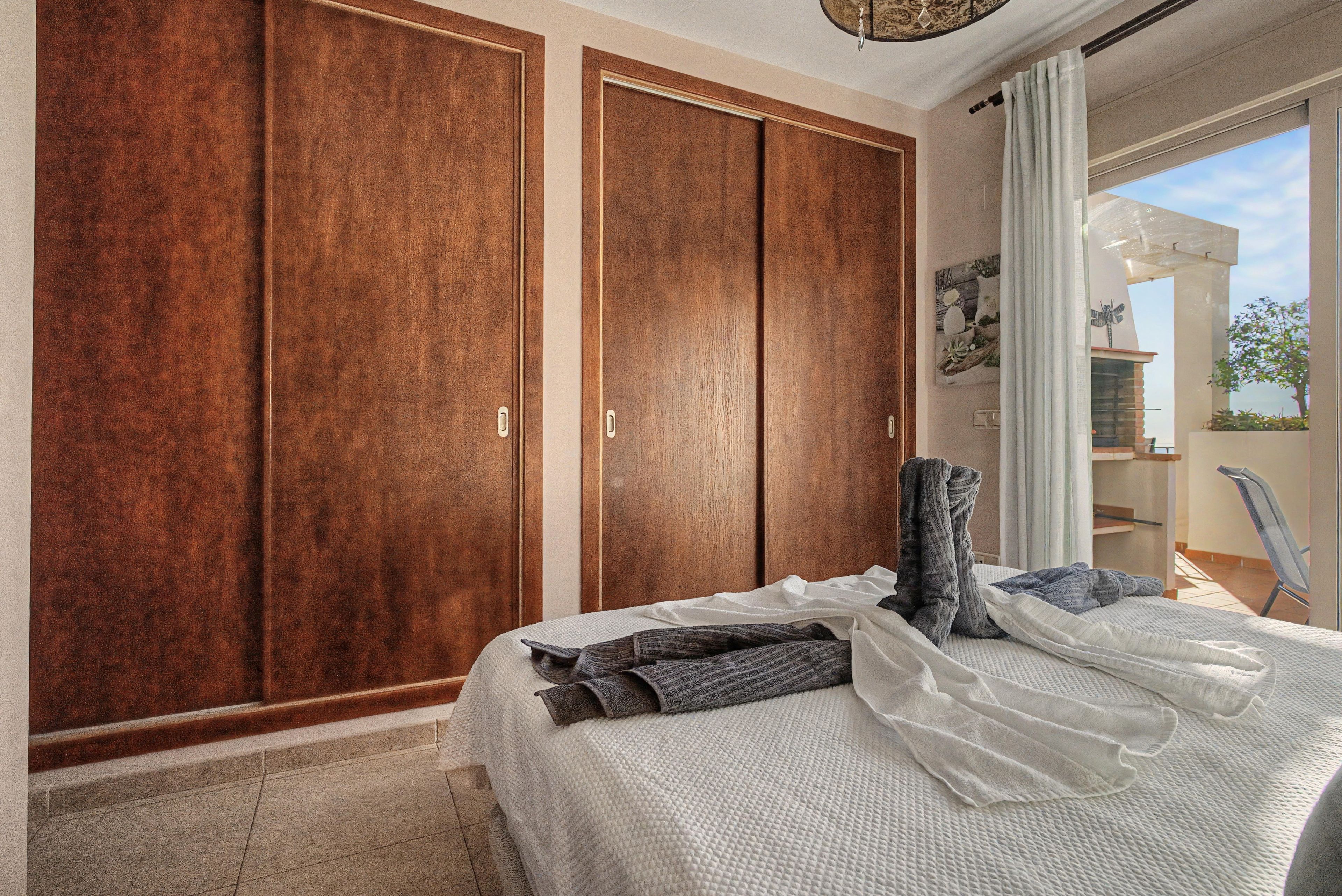 Un dormitorio con un armario grande, una cama con colcha blanca texturizada y vistas al exterior a través de una ventana.