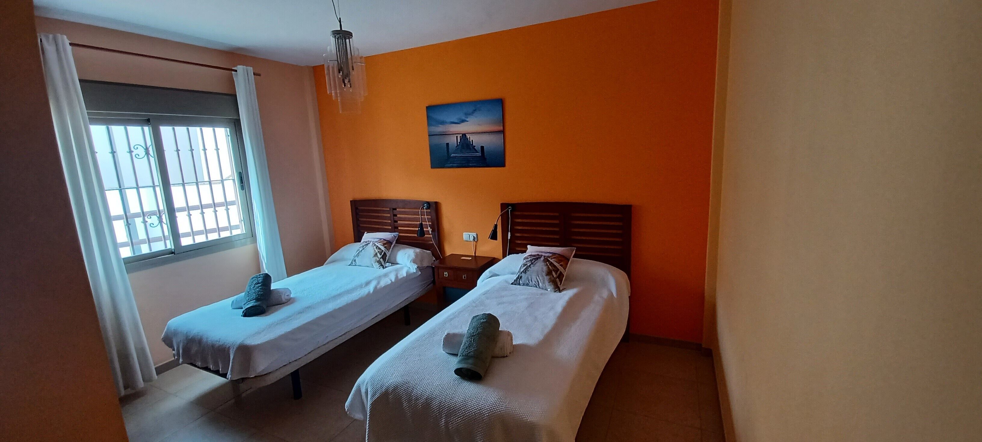 Una habitación con dos camas, una ventana con cortinas, un cuadro en la pared y un candelabro.