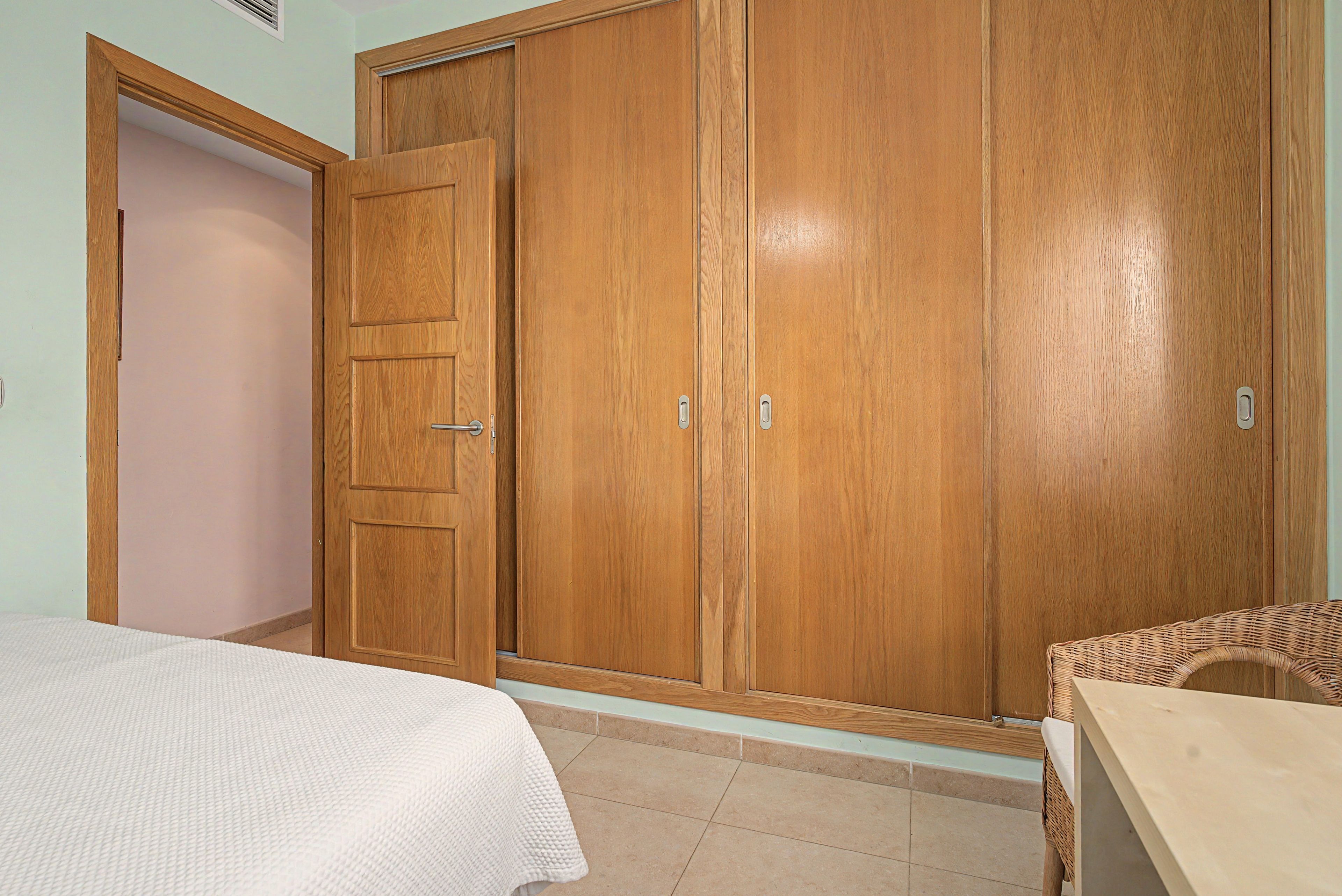 Un dormitorio con cama, armario y una silla de mimbre.