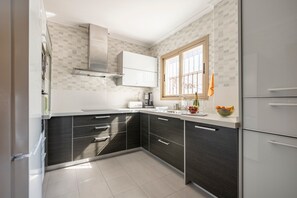 Une cuisine moderne avec des meubles de couleur sombre, un plan de travail blanc, une fenêtre et un four encastré.