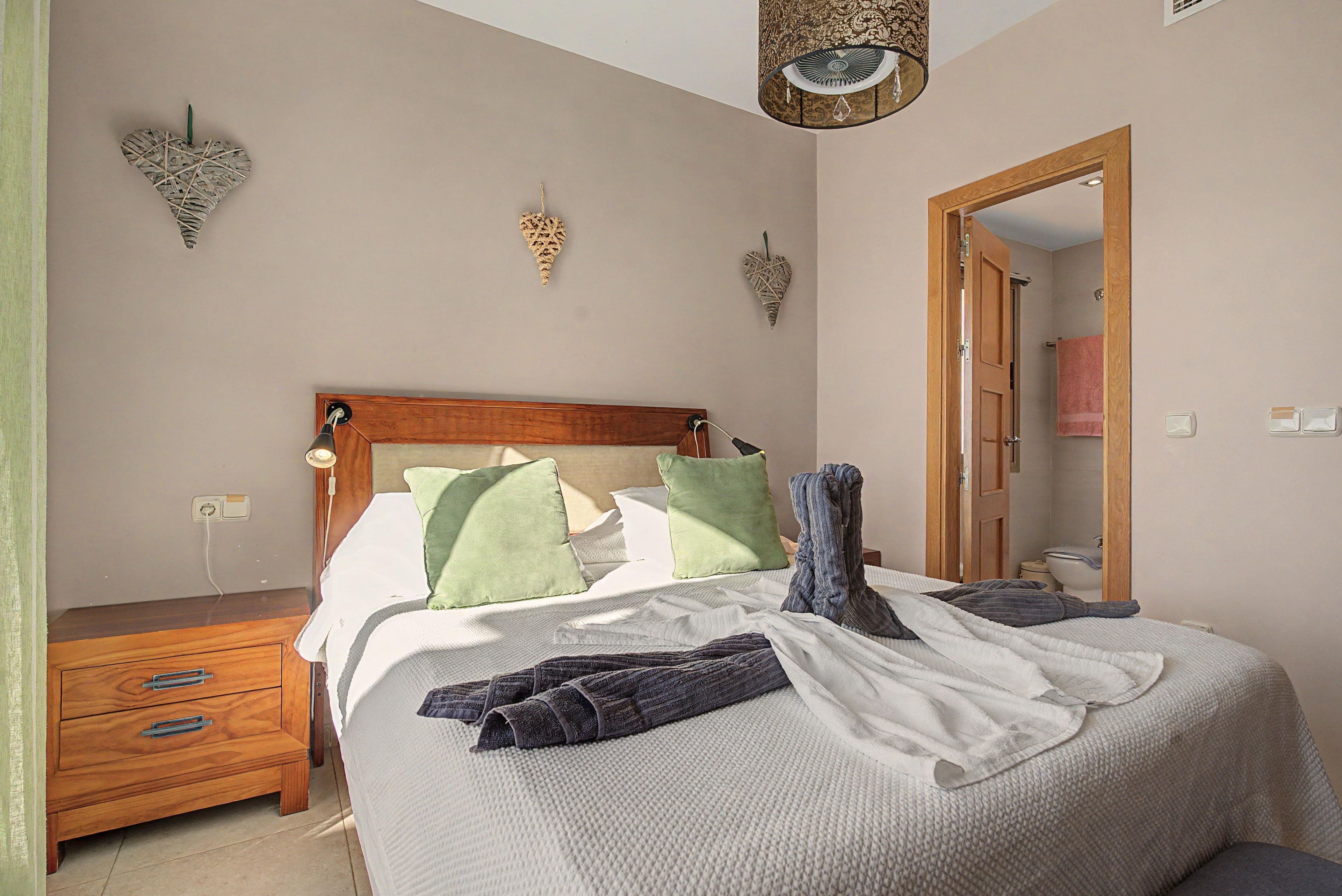 Un dormitorio con cabecera de madera, una mesita de noche, una lámpara colgante y una puerta de madera que da a un baño.