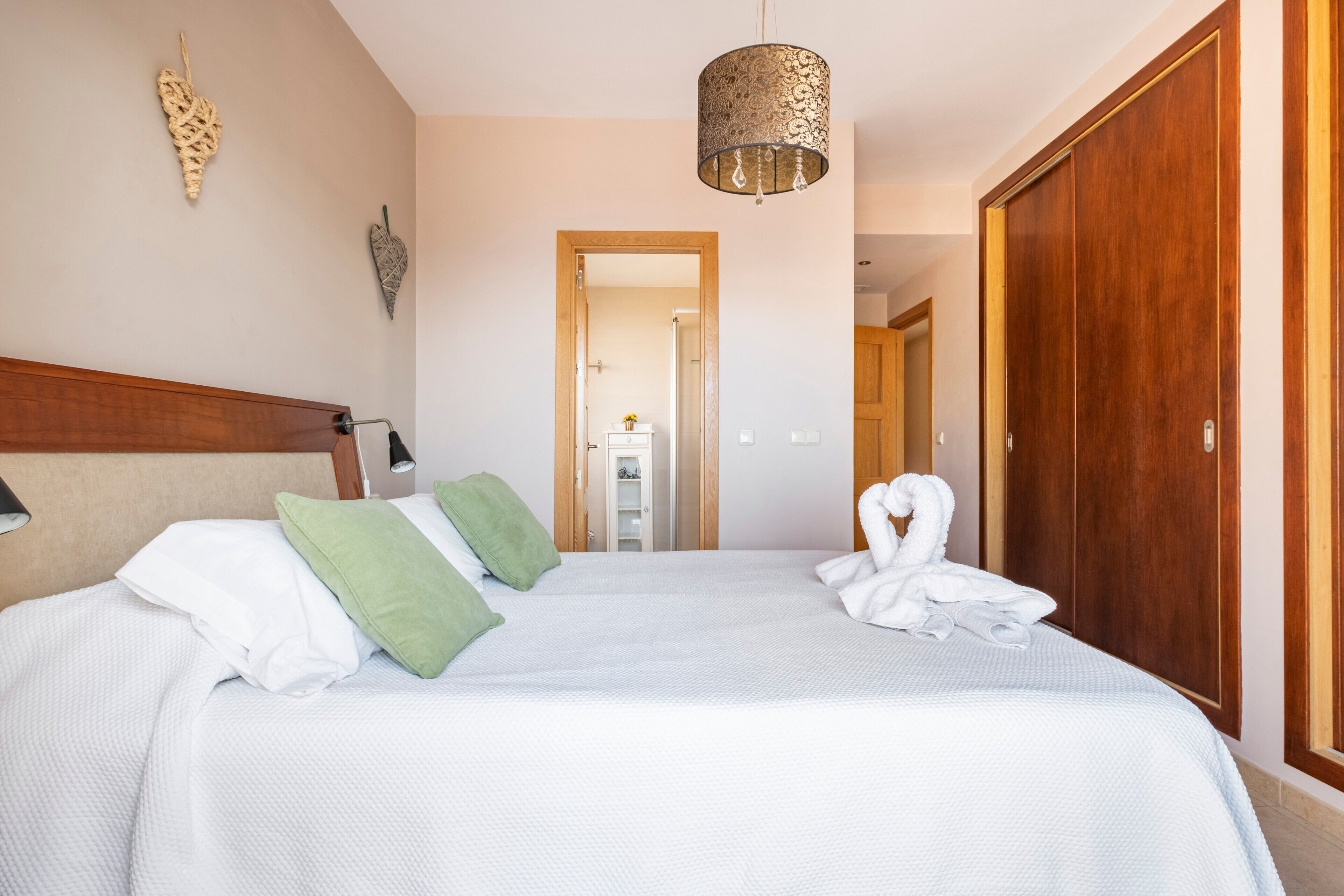 Un lit bien fait, avec des oreillers, un luminaire suspendu et une armoire en bois.