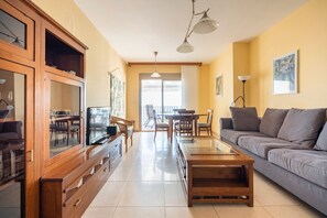 Un soggiorno con divano, tavolino, televisione, mobiletti in legno e zona pranzo con sedie e tavolo.