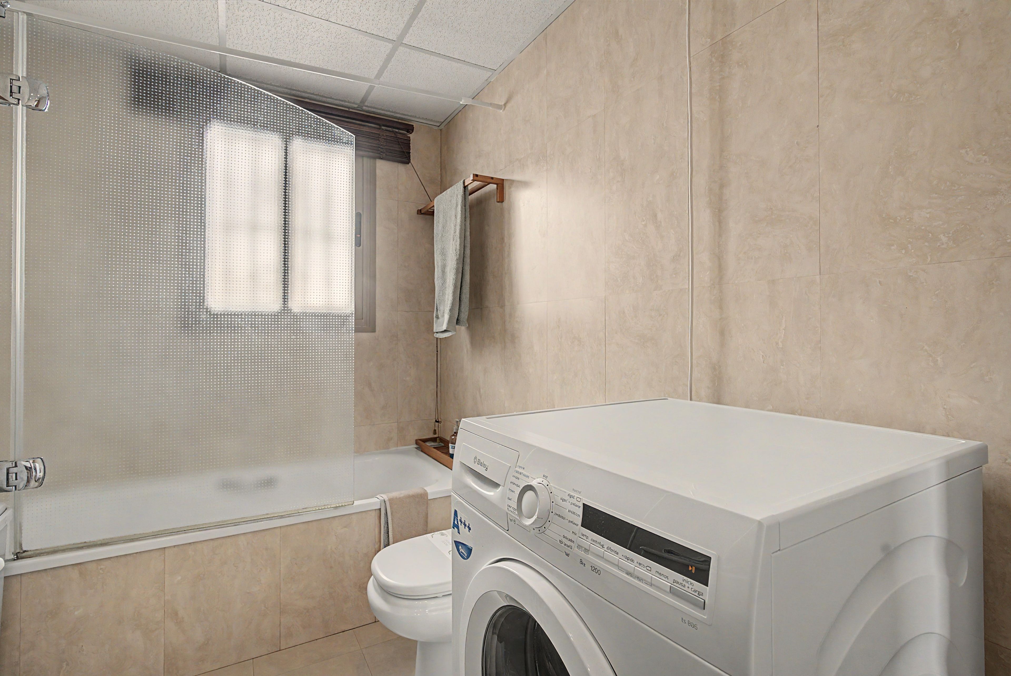 A compact bathroom with a shower enclosure, a toilet, and a front-loading washing machine.