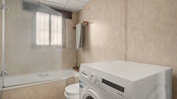 A compact bathroom with a shower enclosure, a toilet, and a front-loading washing machine.