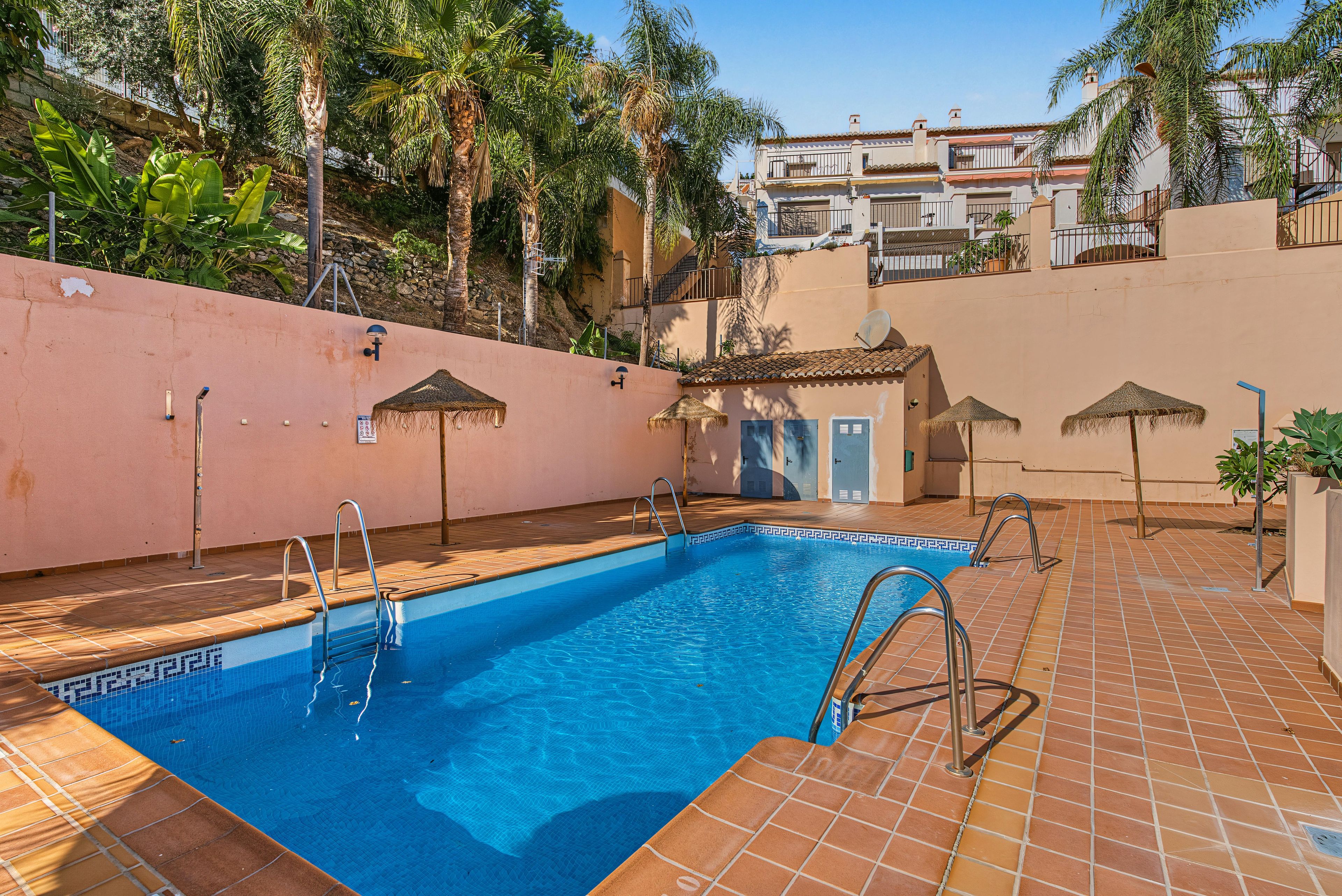 A swimming pool with a tiled deck, metal pool ladders, and a clear blue pool.