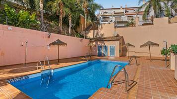 A swimming pool with a tiled deck, metal pool ladders, and a clear blue pool.