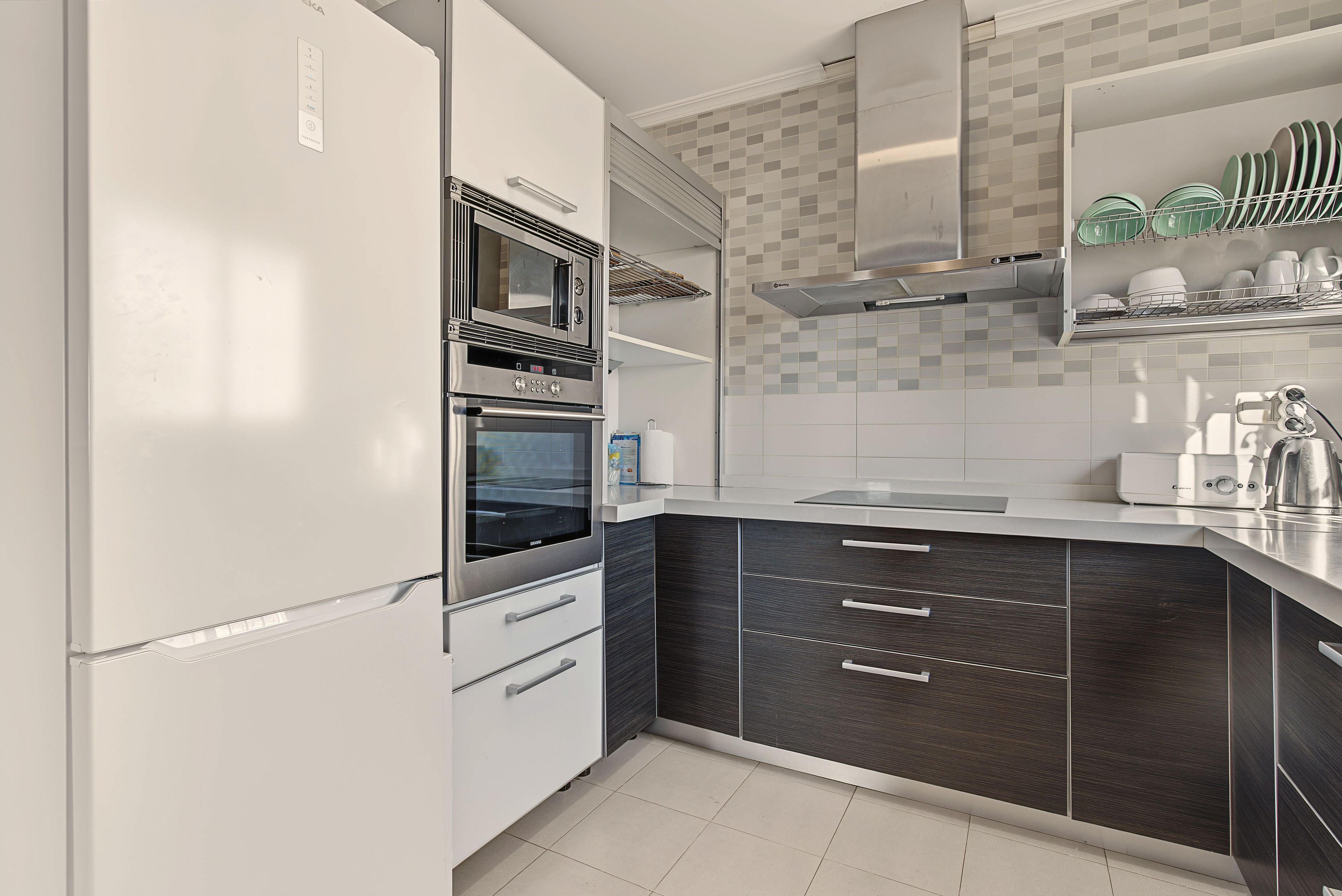 Una cocina moderna con horno empotrado, microondas y campana extractora de acero inoxidable.