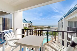 Een balkon met een tafel en stoelen, met uitzicht op een strand en een zwembad.