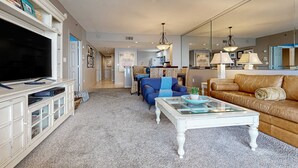 Un salon comprenant un téléviseur, un meuble de rangement blanc, un canapé bleu, une table basse en verre et un divan en cuir marron.