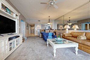 Un salon comprenant un téléviseur, un meuble de rangement blanc, un canapé bleu, une table basse en verre et un divan en cuir marron.
