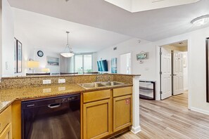 A modern kitchen with granite countertops, a dishwasher, and wooden cabinets. - Gorgeous coastal condo with balcony & resort pools - close to beach (Destin)